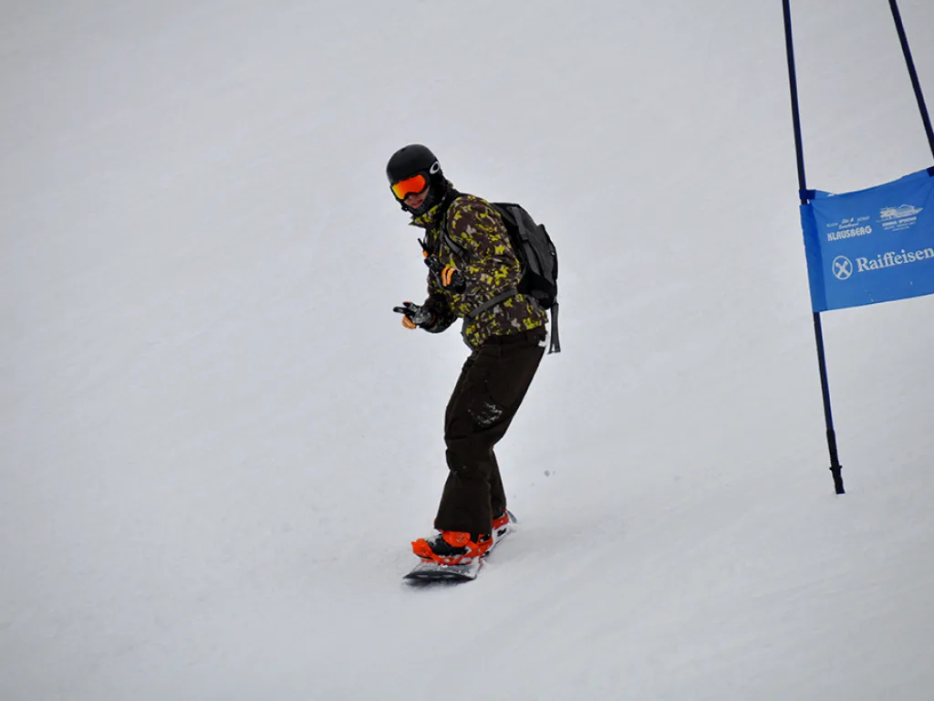 Snowboarder in gemusterter Jacke neben dem blauen Tor.